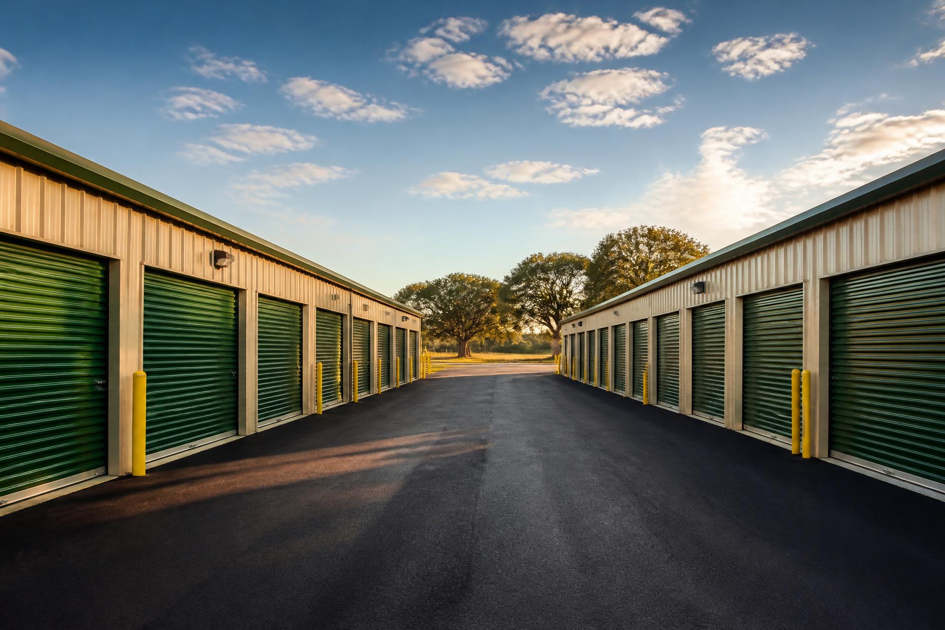 Clean drive lane between tan storage buildings with green roll-up doors at Highway 71 Storage in Cedar Creek, Texas